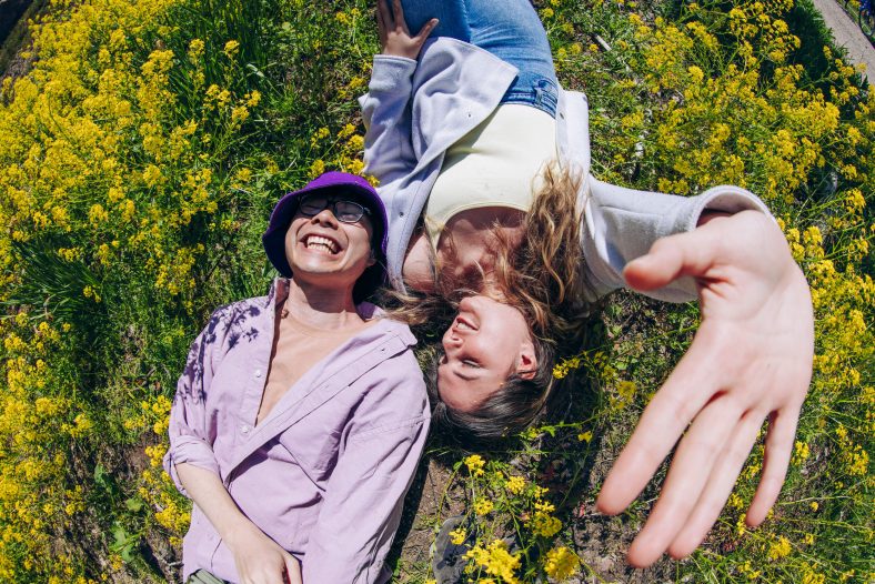 Two students laughing and lying on a floral field